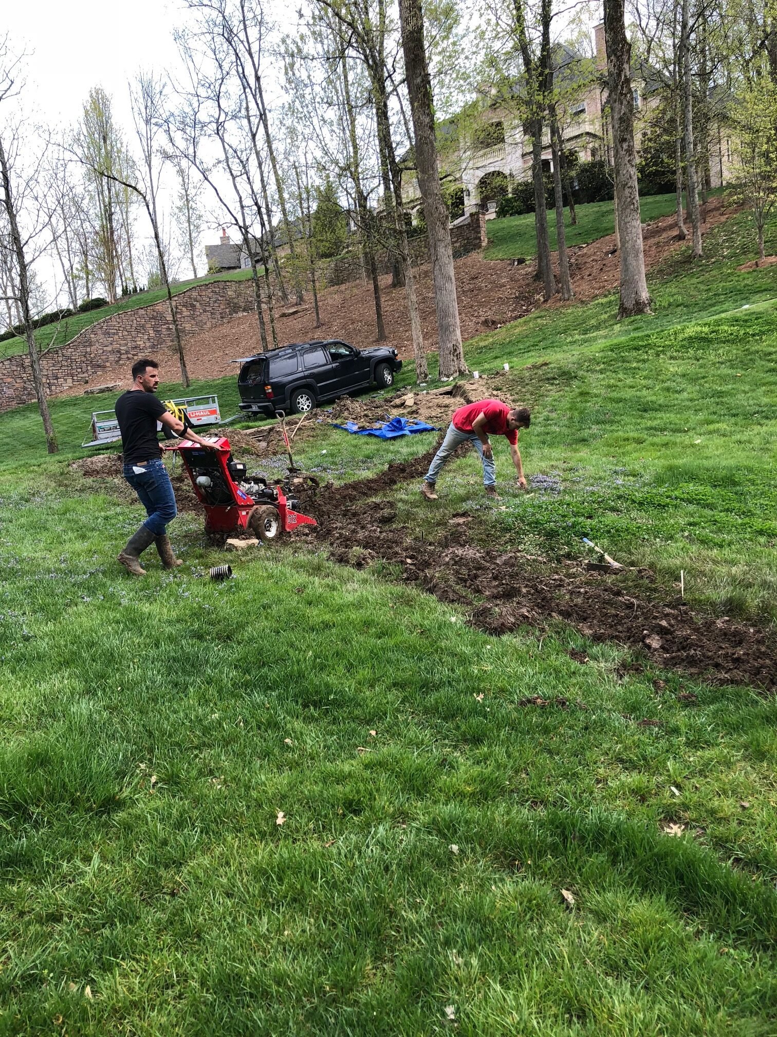 Two workers digging a trench in a grassy yard with a trencher for drainage installation
