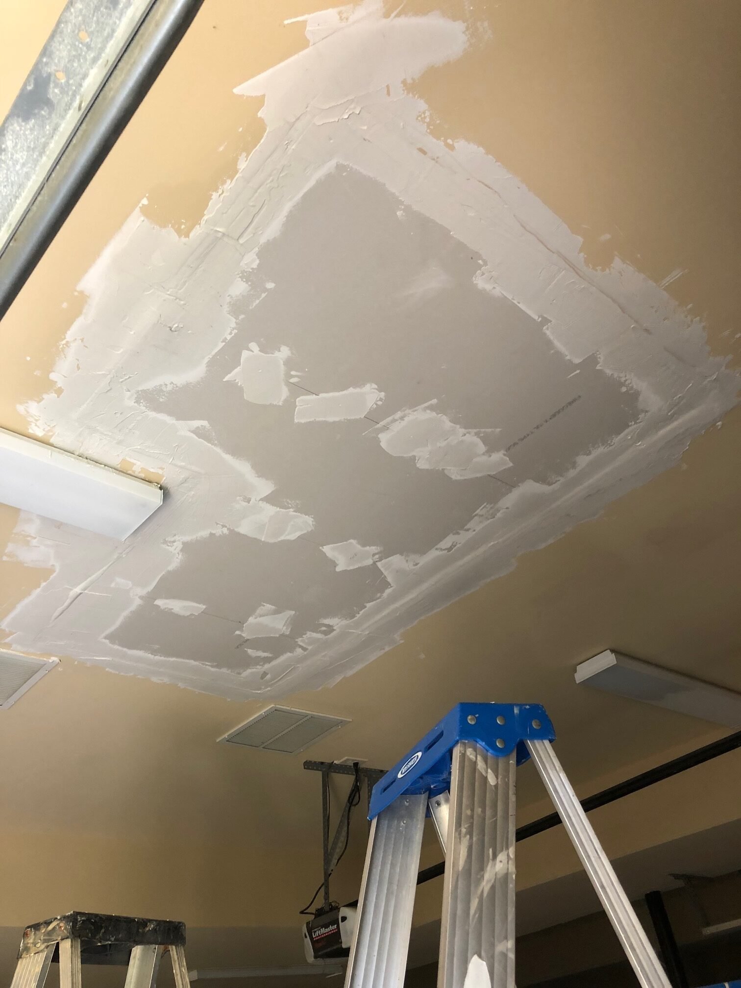 Drywall ceiling repair in progress with patched seams and ladder below