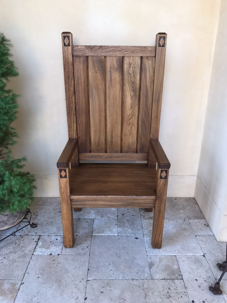 Restored wooden chair with intricate joinery placed against a light wall and stone floor