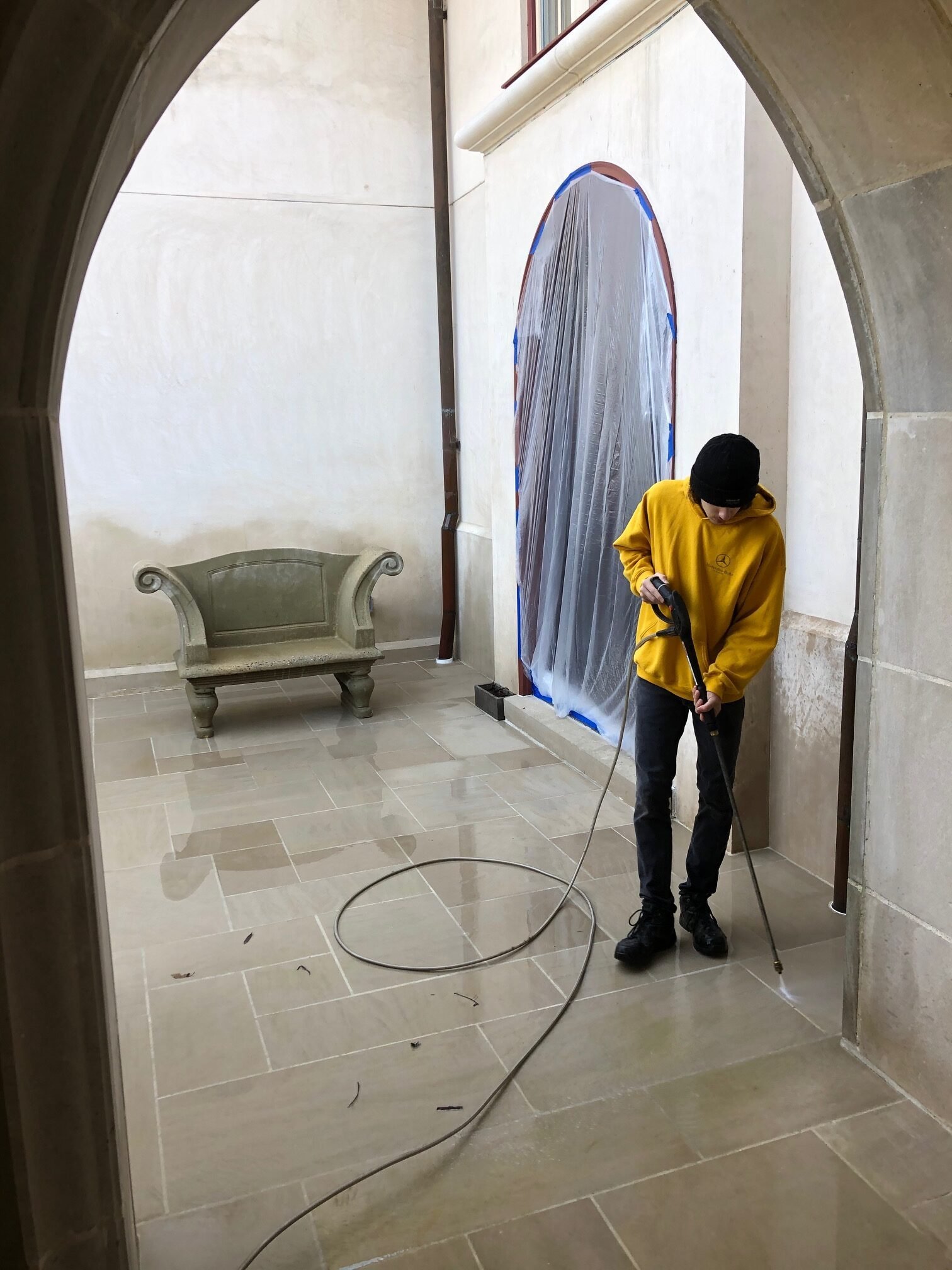 Worker power washing a stone patio or floor indoors with a hose and pressure washer