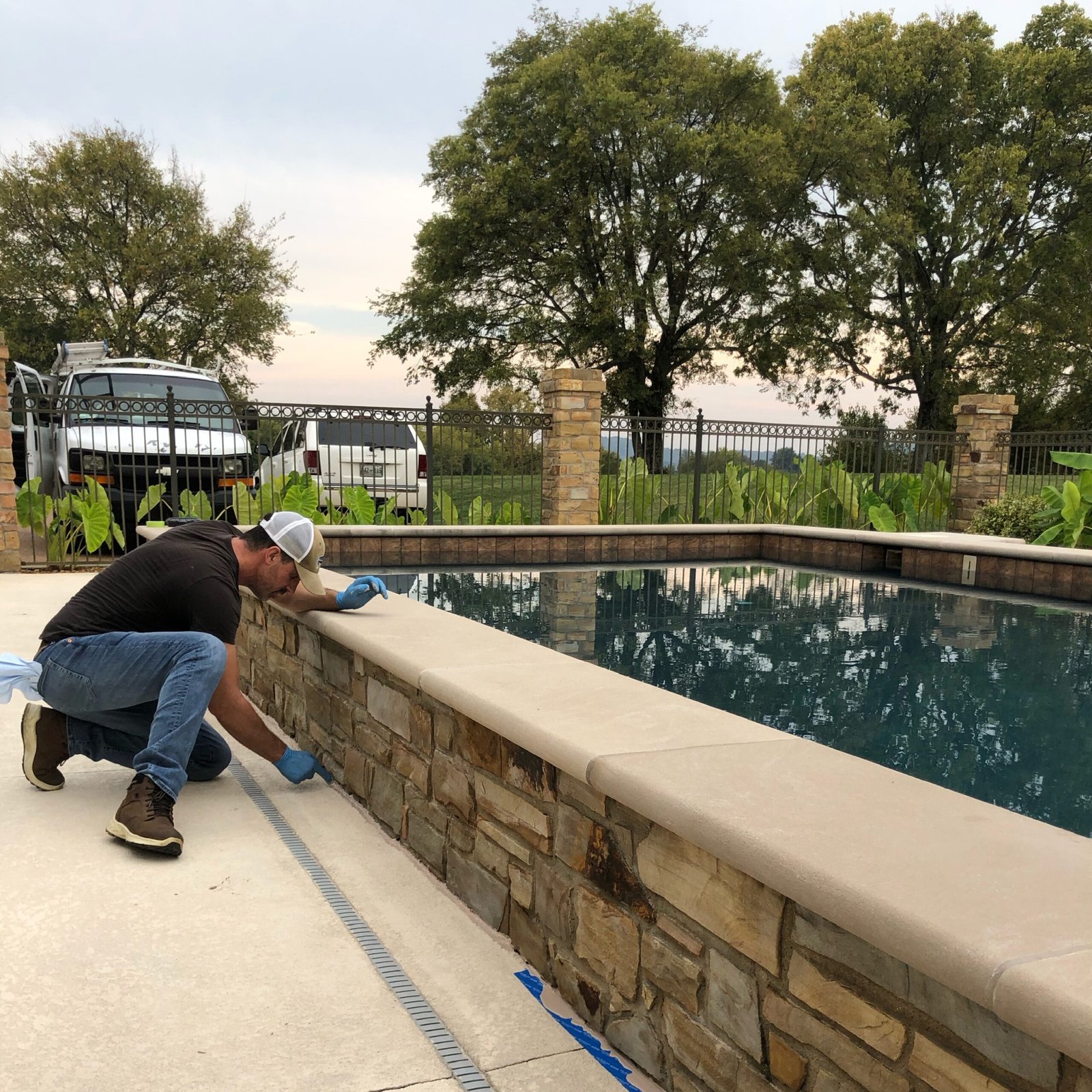 Home Handyman applying sealant along a stone pool wall at a residential property